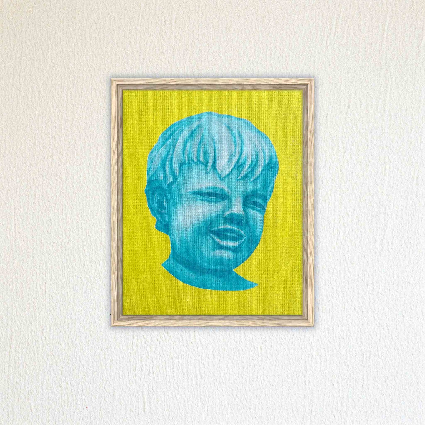 Framed artwork of a blue face on a yellow background, mounted on a textured white wall.