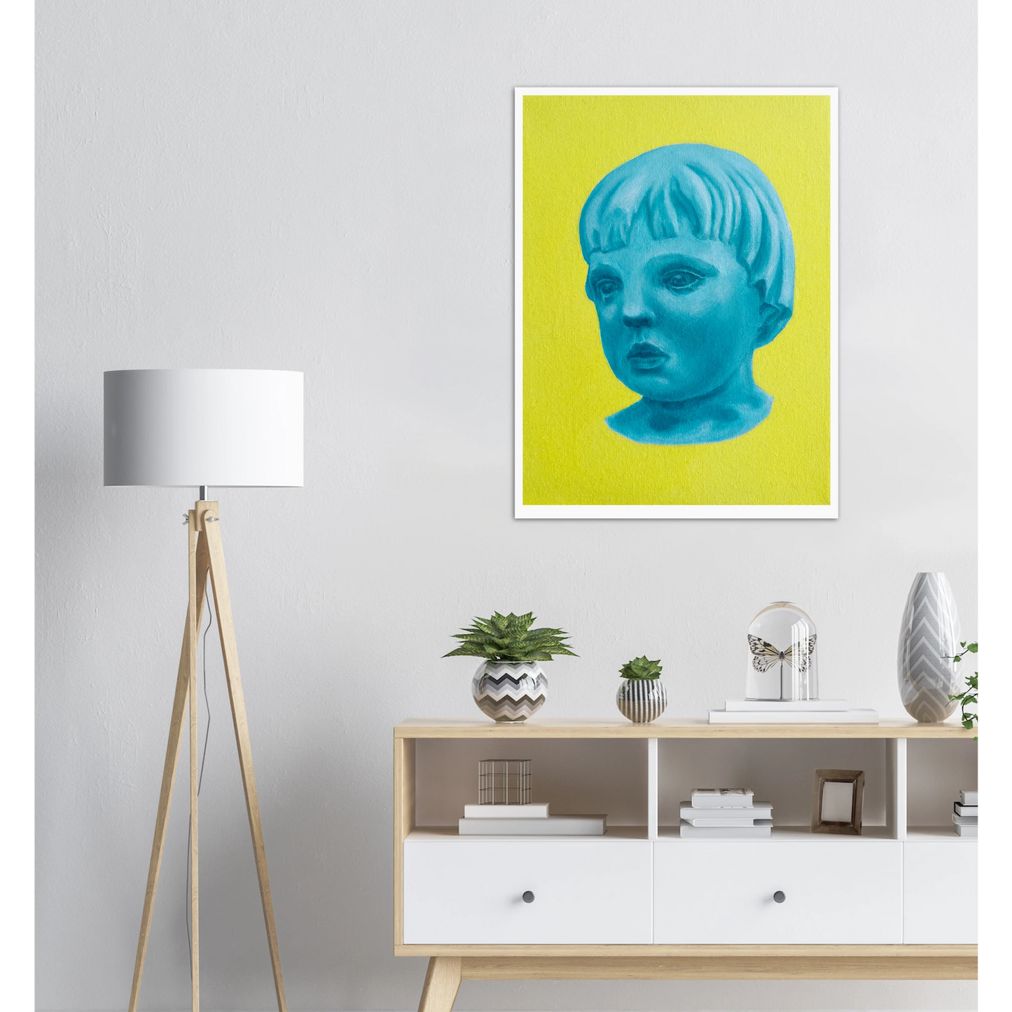 Artwork of a blue face on a yellow background above a white cabinet with decorative items.