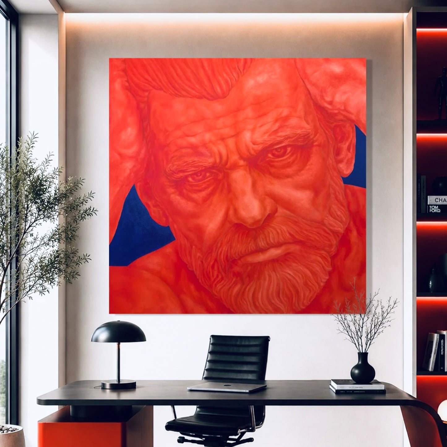 A large square wall art print featuring a stylized red portrait of a bearded man with blue background accents, displayed above a black desk in a modern office interior.